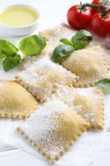 Uncooked ravioli, basil, tomatoes and oil on white wooden table, closeup