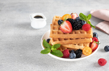 Crispy Belgian waffles with fresh berries and maple syrup on a gray background. Close-up, copy space.