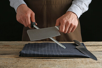 Man sharpening knife with sharpener on wooden table, closeup