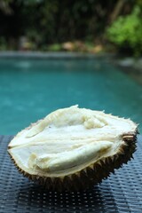 Fresh ripe durian on wicker table near swimming pool outdoors, closeup