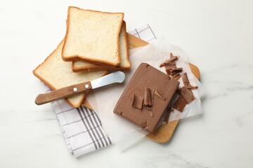 Block of tasty chocolate butter, bread slices and knife on white marble table, top view