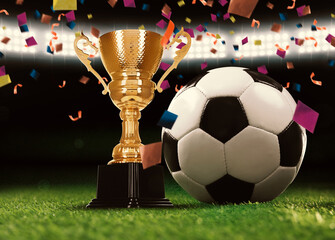 Football championship. Shiny golden trophy cup and soccer ball under falling confetti on stadium