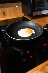 A close-up shot of a fresh egg cooking in a black skillet. The yolk is vibrant and runny, while the egg white gently bubbles as it fries on medium heat.

