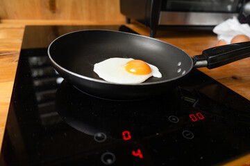 A close-up of a sunny side up egg frying in a sleek black pan. The yolk glows bright yellow while the whites cook gently, creating a perfect breakfast moment.

