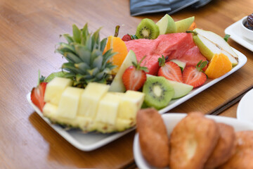 A large plate of fresh fruits arranged on a wooden table during a hotel breakfast experience
