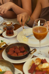 Close-up of a woman's hands cutting cheese with knife and fork at a hotel breakfast table set with salad, tea, and cheese. Pool visible in the background