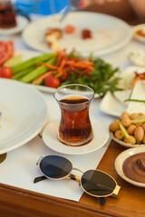 A traditional Turkish tea sits on a wooden table as part of a hotel breakfast. Sunglasses rest nearby, adding a relaxed vacation feel to the warm morning setting