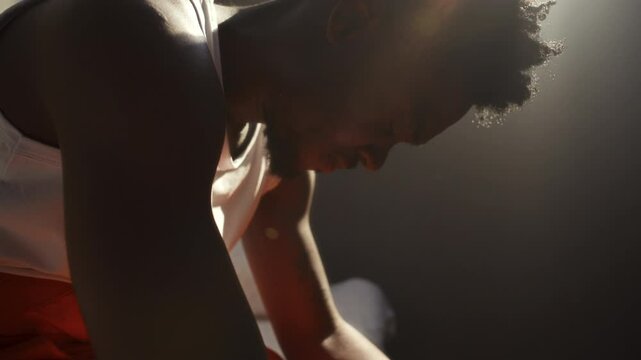 Young African American inmate sitting in sunlit prison cell, suffering from emotional distress and anxiety. Close-up view