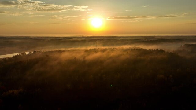 Beautiful dawn aerial shot of sunlight shining thought the trees and low fog in Minnesota in the autumn. Trees are turning their fall colors