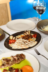 Delicious meat plates presented on white-clothed table during elegant hotel dinner with swimming pool in background view
