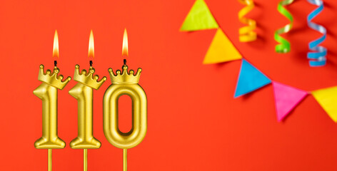 Number 110 birthday candle on an orange background with pennants
