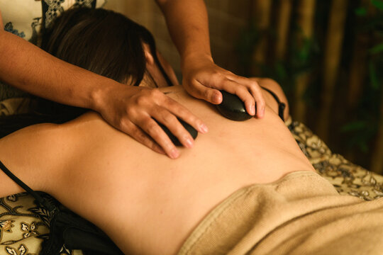 Professional therapist performing soothing hot stone massage treatment on woman's back in elegant hotel spa - Powered by Adobe