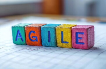 Colorful wooden blocks arranged to spell the word agile on a white grid-lined surface with a soft blurred background