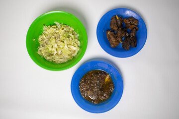 Traditional home-cooked food with spicy chili sauce, stir-fried cabbage and crispy chicken innards on a blue and green plate.