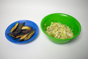 A simple dish of stir-fried cabbage in a green bowl and fried eggplant slices on a blue plate,...
