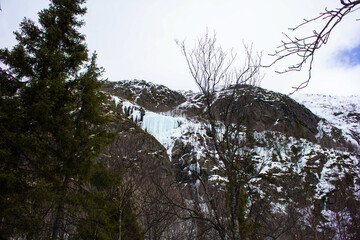  Frozen waterfall cascading down a rocky mountain slope covered with snow and ice. Winter...