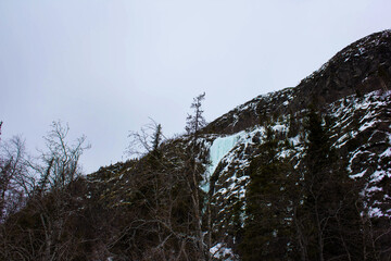  Frozen waterfall cascading down a rocky mountain slope covered with snow and ice. Winter...