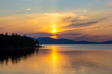 Stunning sunset over a calm lake with golden reflections, mountains on the horizon, and forest silhouette. Perfect for travel, nature backgrounds, peaceful landscapes, eco tourism, and inspiration.