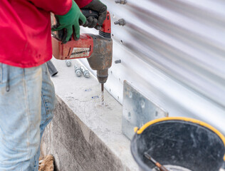 The worker is using a cordless drill to drill into the concrete floor to secure the plate.