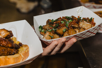 Close-up of roasted cubed potatoes topped with bacon bits and sliced green onions served in a paper...