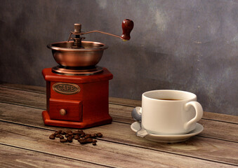 A manual coffee grinder, fried grains and a cup of freshly brewed black coffee on a wooden table.