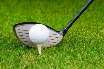 Close up of golf ball on tee with driver behind it.
