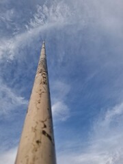 A tall, slender pole, possibly a flagpole or utility pole, reaching up towards a bright blue sky...