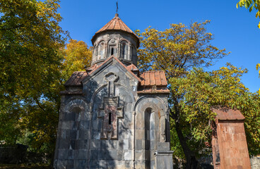 Ancient stone Mashtots Hayrapet Church with a dome and cross, surrounded by trees with autumn...
