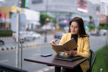 Fototapeta premium Businesswoman working remotely at outdoor cafe, taking notes in notebook