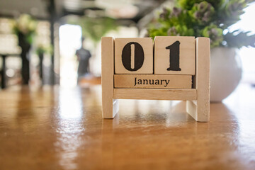 Cube shape calendar for January 01 on wooden table. Wooden calendar with blur cafe background