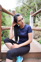 Chica bonita morena, sentada en un puente mientras compone su cabello luego de hacer su rutina de...