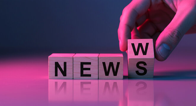Hand Placing Wooden Block Completing the Word News in Pink and Purple Lighting