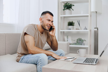 Young man smiling while talking on the phone at home, casually dressed, surrounded by cozy decor. A modern workspace creates a relaxed atmosphere for productivity.