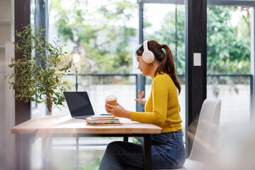 Happy asian girl college student wearing headphones watching distance online class, remote university webinar or having talk on laptop video conference call virtual meeting at home or campus.

