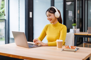Portrait of Young Asian woman sitting at desk and connecting with her laptop, she is wearing...