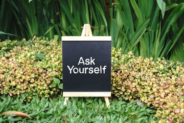 Ask Yourself writing concept on a small blackboard with a background of trees.
