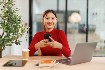 Shot of a asian young business Female working on laptop computer and holding phone in her...