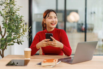 Shot of a asian young business Female working on laptop computer and holding phone in her...