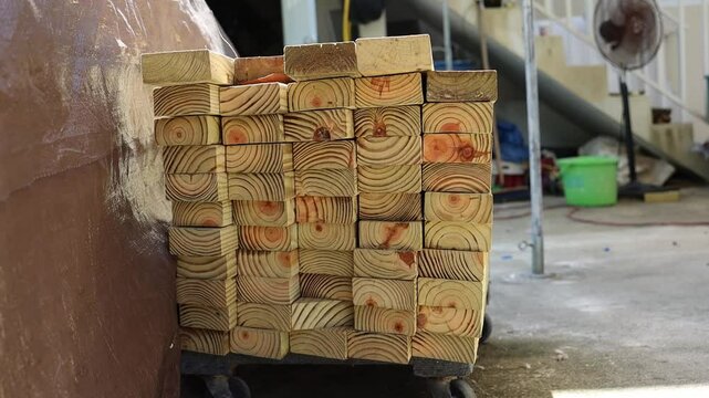 Stack of freshly cut wooden beams neatly piled on a cart in a shaded construction site or workshop