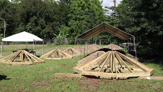 Bohio-style wooden frames lie under canopy tents, prepared for traditional structure assembly