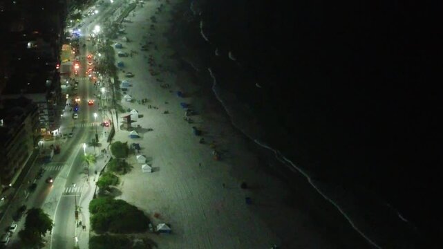 Aerial night view of Praia do Forte in Cabo Frio, Brazil, with illuminated sand and shoreline. The beach glows under city lights, creating a stunning coastal scene after sunset.