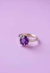Gold ring with vibrant purple gemstone displayed on pastel pink background, exuding elegance and charm