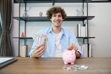 young man putting money into piggy bank and holing banknotes at home
