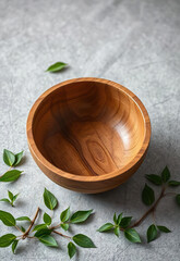 Handcrafted wooden bowl with smooth finish, surrounded by green leaves on textured gray surface