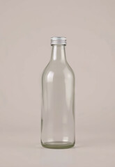 Clear glass bottle with silver metal screw cap, standing upright neutral beige background. bottle is empty and has simple