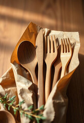 Eco friendly wooden cutlery set with spoons, forks, and knives on brown paper, illuminated by warm natural light