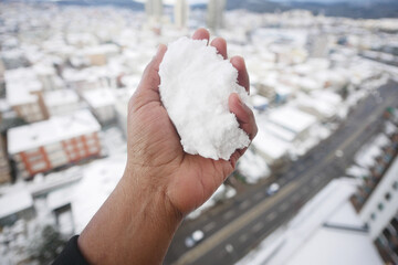 Snow gathered in hand against a snowy city backdrop