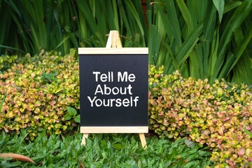 Tell Me About Yourself writing concept on a small blackboard with a background of trees.
