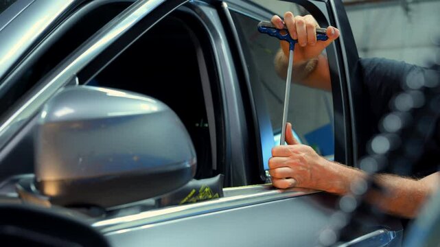 Process of pointless dent repair on car body, mechanic at the auto shop with tools to repair dents in car body. PDR. Close up