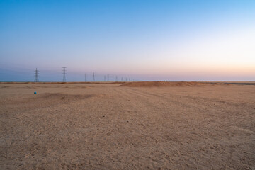 The tranquil Aswan desert in Egypt at dawn, featuring a gentle sunrise glow and a series of electricity pylons stretching across the vast landscape on the journey to Abu Simbel Temples.